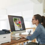 Une femme assise à un bureau, concentrée sur son travail, avec une imprimante Xerox® C320 couleur